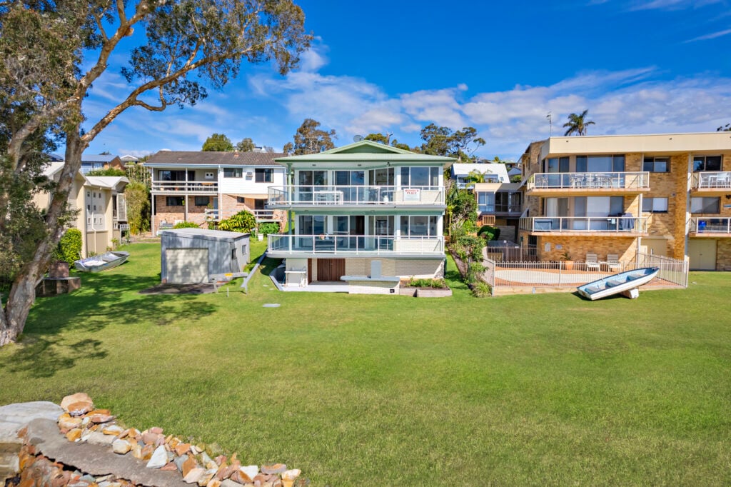 Three-level Woody’s Place building with balconies and lawn viewed from the waterfront at Soldiers Point